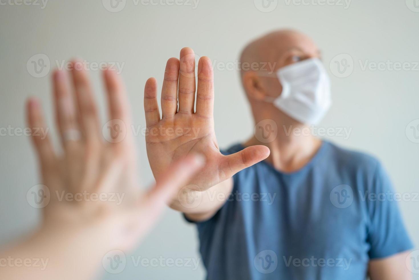 A bald man holds a medical mask in his hands, his other hand held out in protest photo
