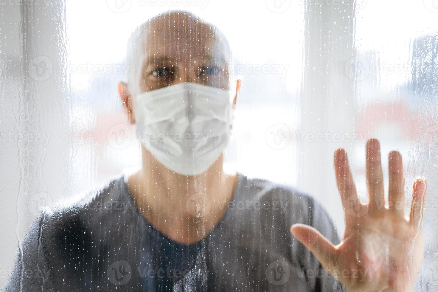 portrait of a man in a protective mask looks through the windows to the street photo