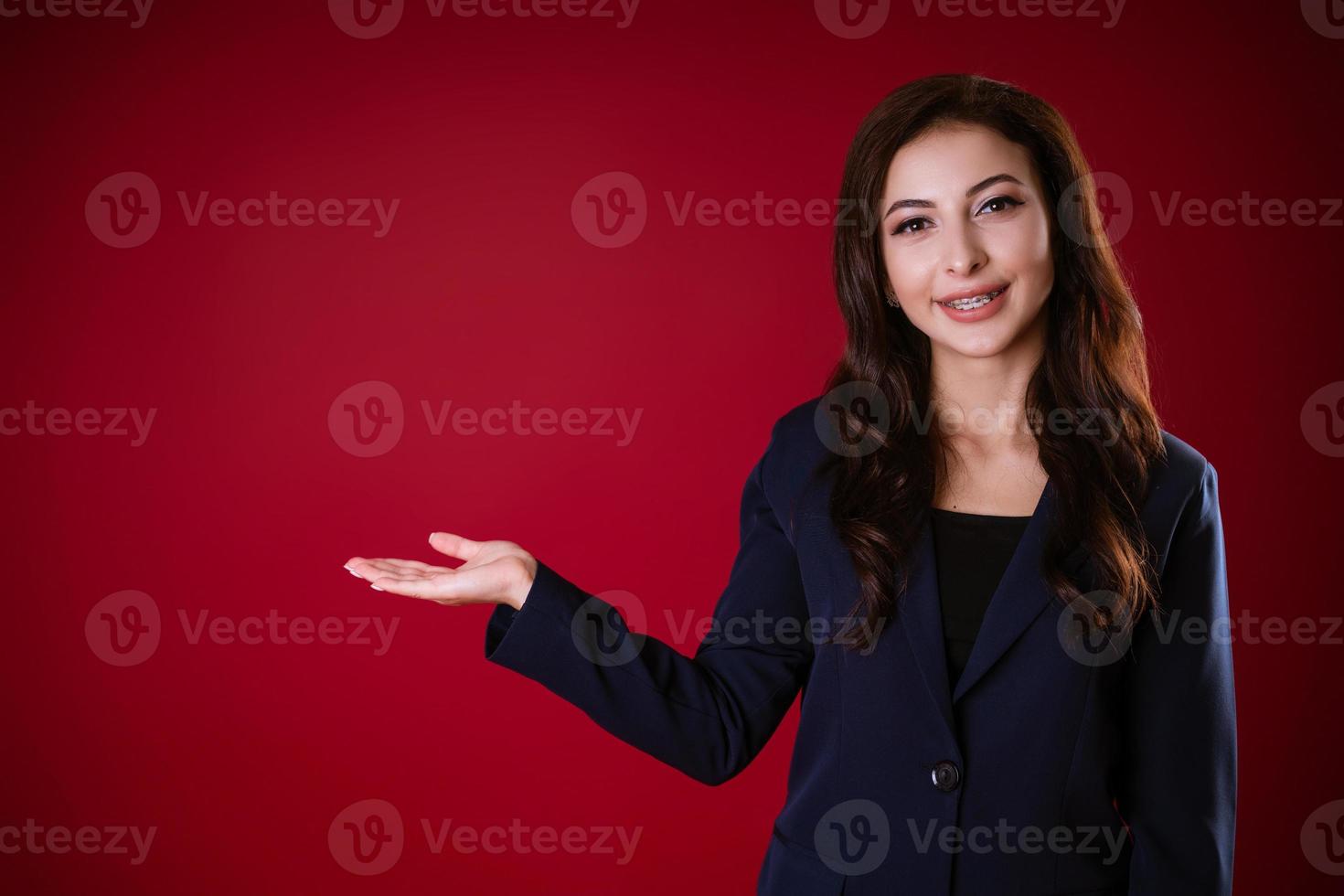 Beautiful business woman on a red background holds her hand to the side photo