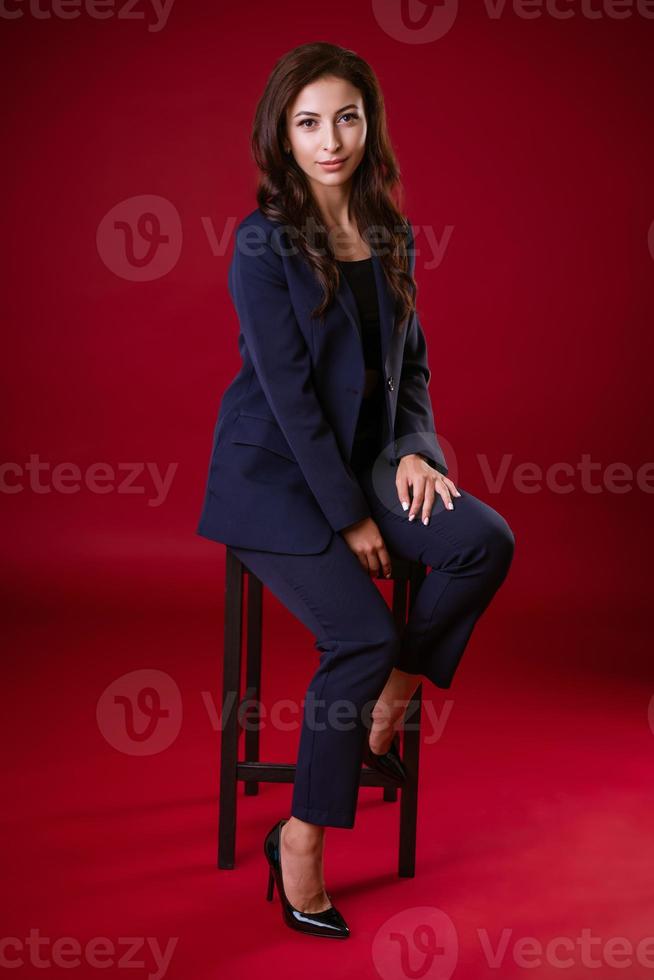 Business woman in suit posing on chair on red background photo