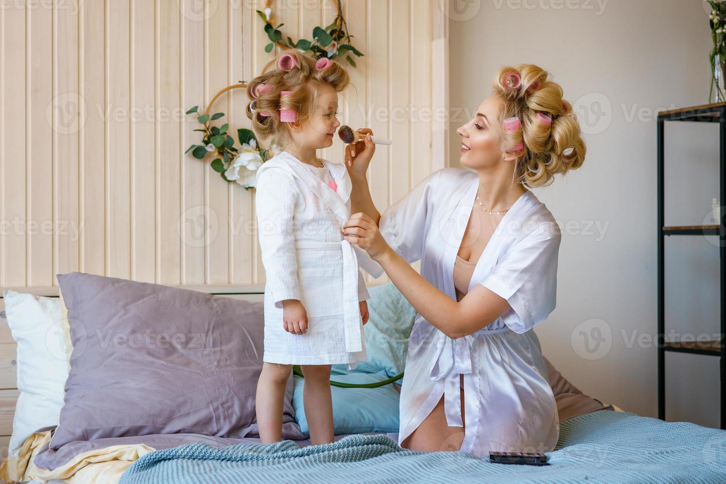 mom and daughter in curlers , make a make-up to each other, a happy family photo