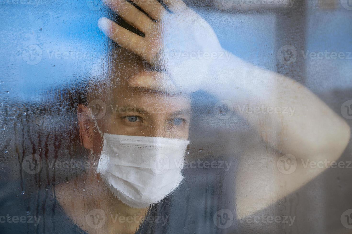 portrait of a man in a protective mask looks through the windows to the street photo