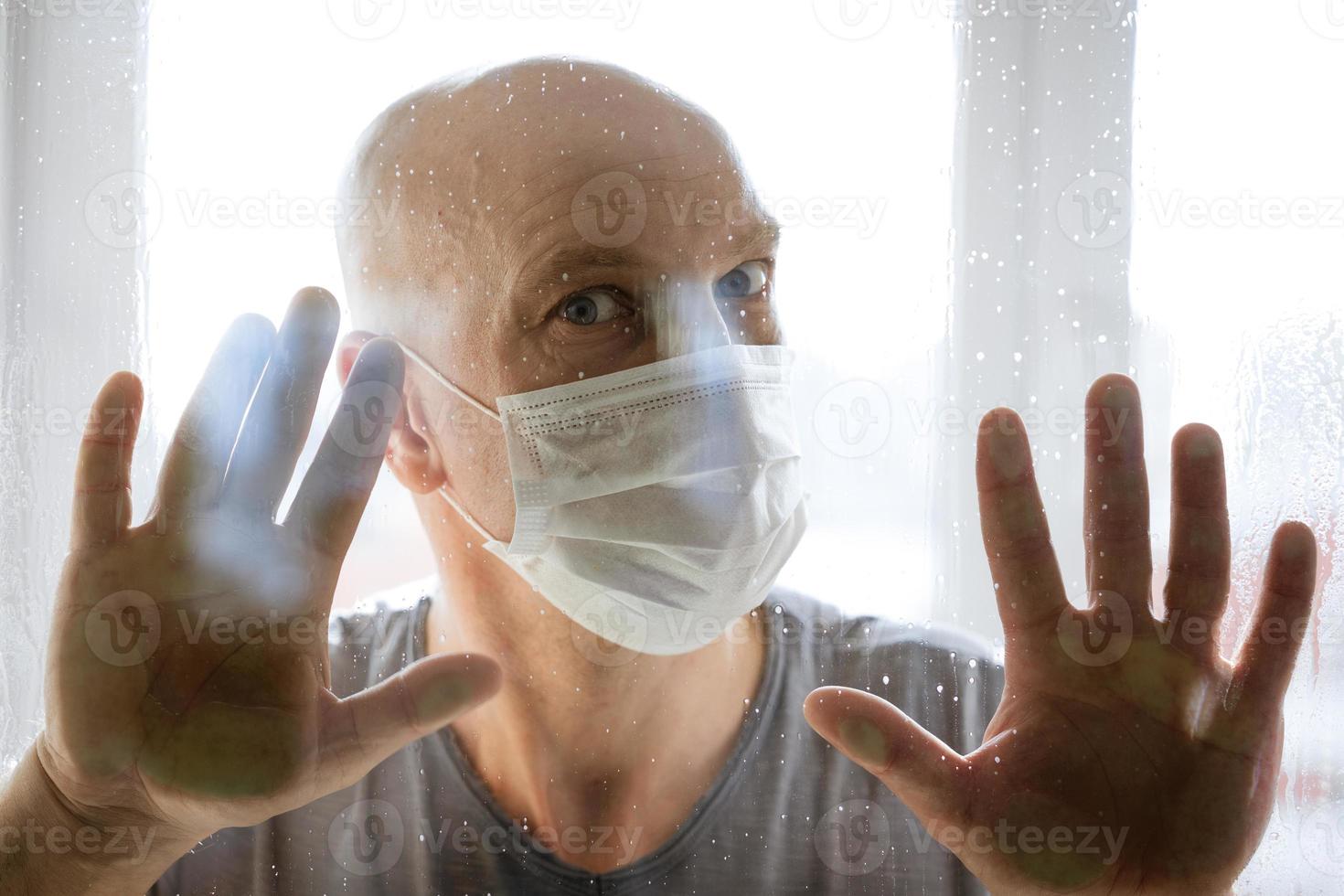 portrait of a man in a protective mask looks through the windows to the street photo