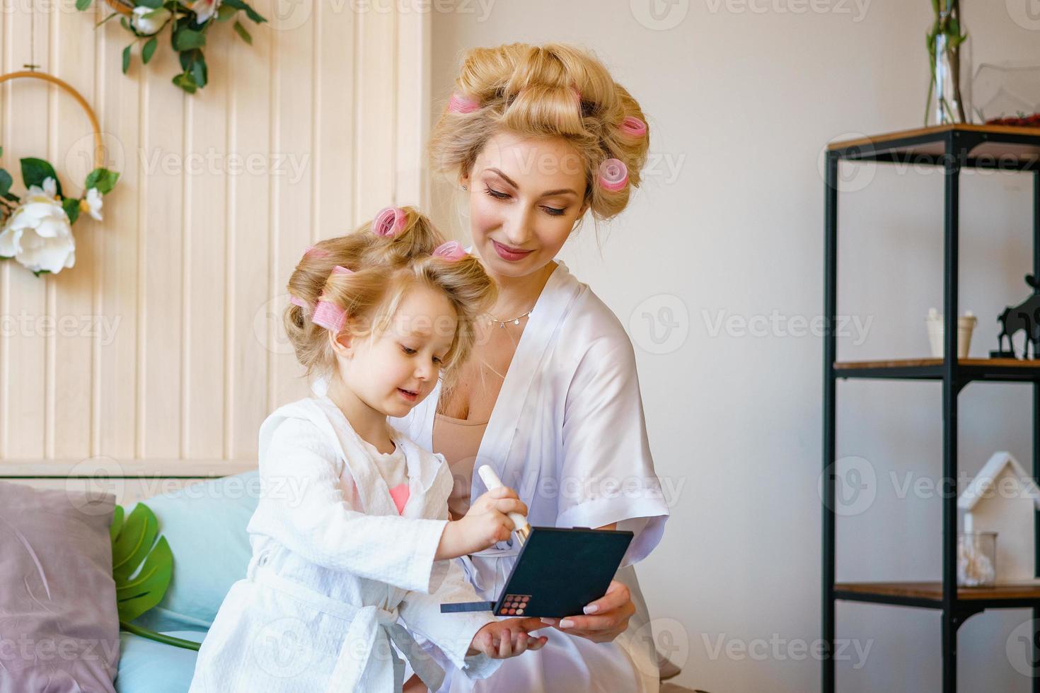 mom and daughter in curlers , make a make-up to each other, a happy family photo