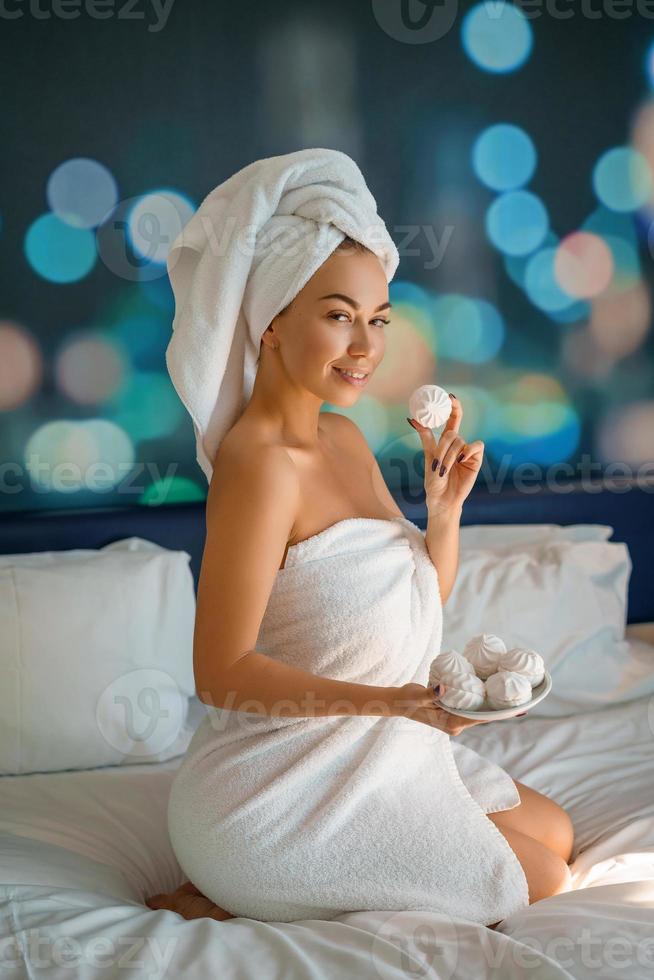 beautiful woman with a towel on her head sitting on the bed and eating