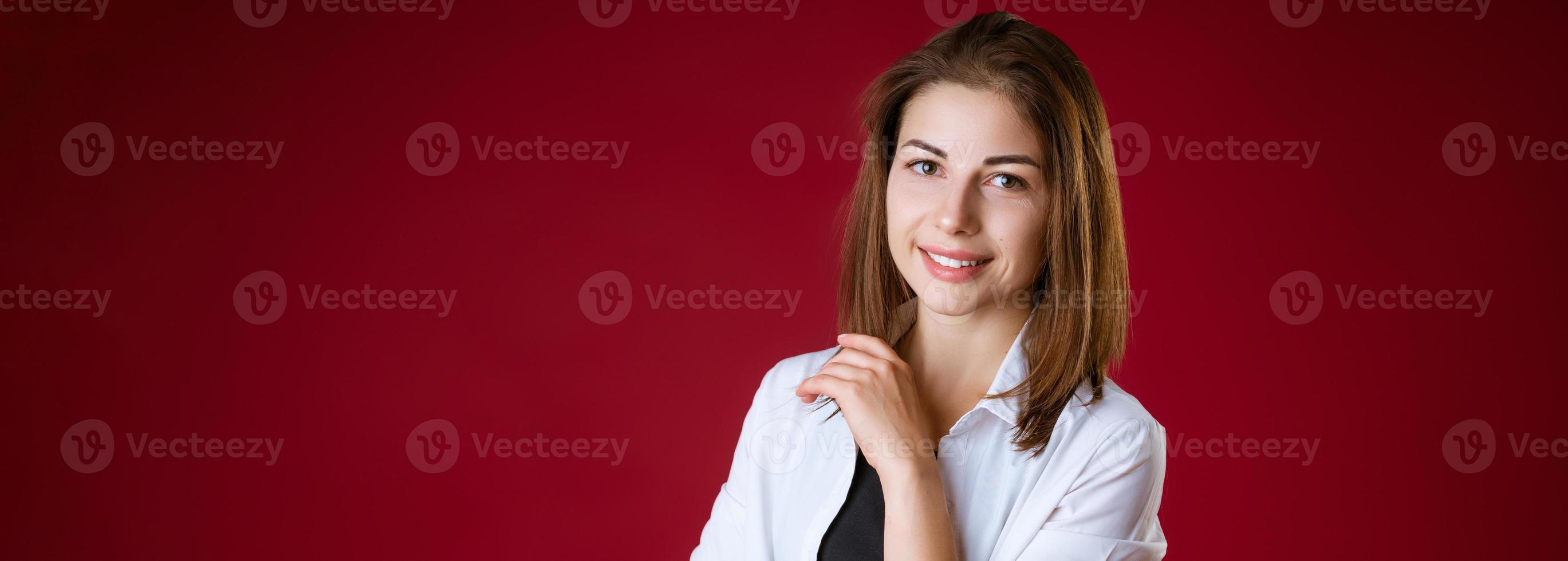 A woman is standing and smiling against a red studio background photo