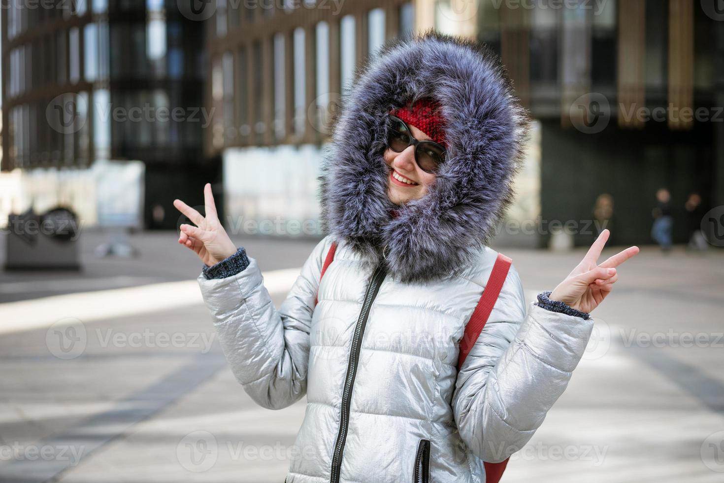 Happy young woman in winter jacket with backpack near building photo