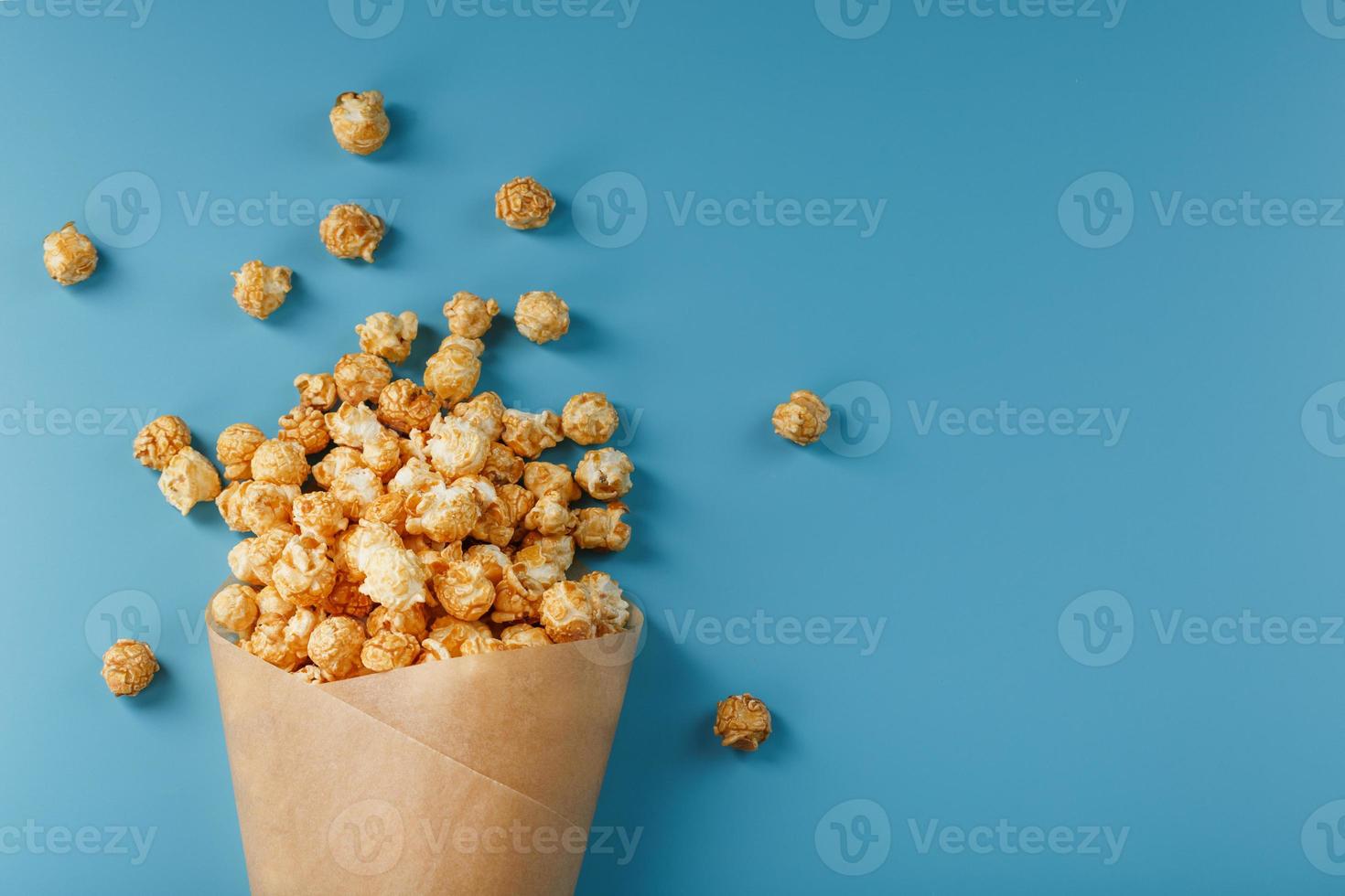 palomitas de maíz en glaseado de caramelo en un sobre de papel sobre un fondo azul. foto