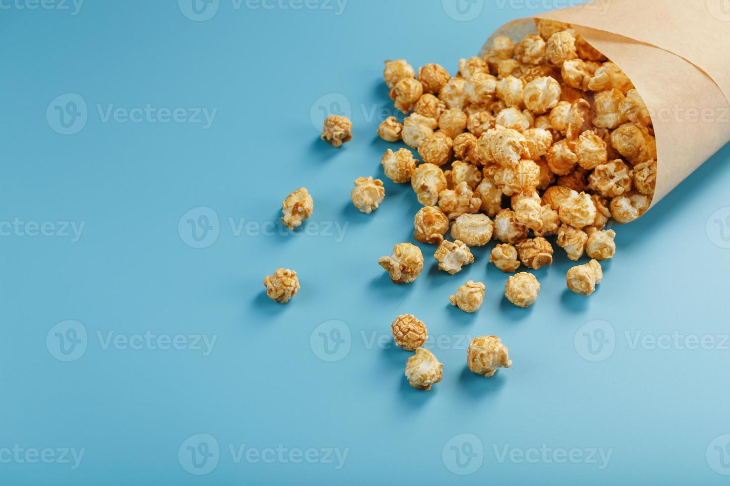 palomitas de maíz en glaseado de caramelo en un sobre de papel sobre un fondo azul. foto