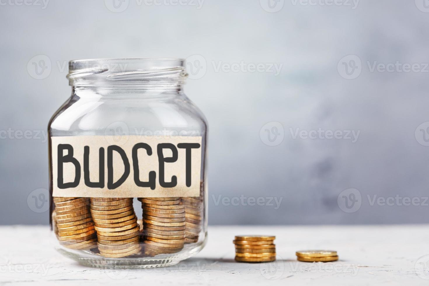 A glass jar with money and the inscription BUDGET, with a sticker with free space for text, on a gray background. photo