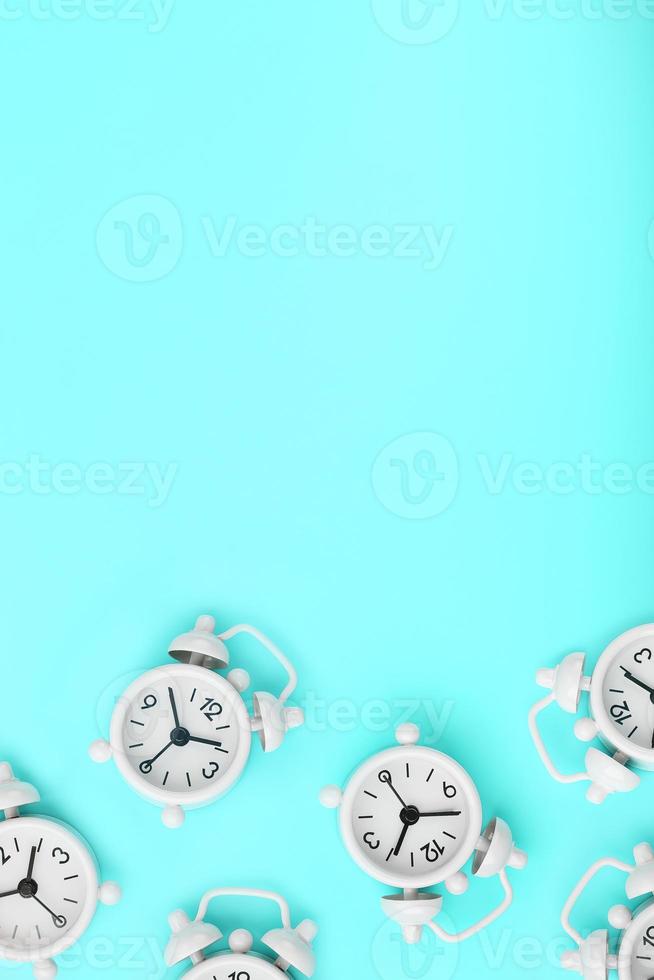 A pattern of many white classic alarm clocks in the form of a pattern on a blue background. Top view with a copy of the space, flat lay. photo