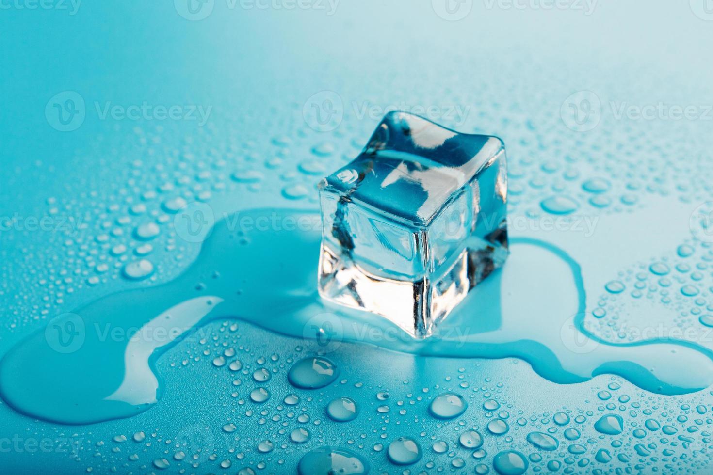 Ice cube with water drops on a blue background. The ice is melting. photo