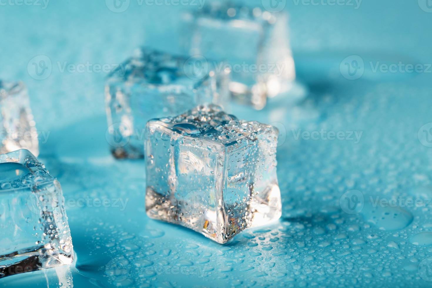 Ice cubes are scattered with water drops scattered on a blue background. Close up. photo