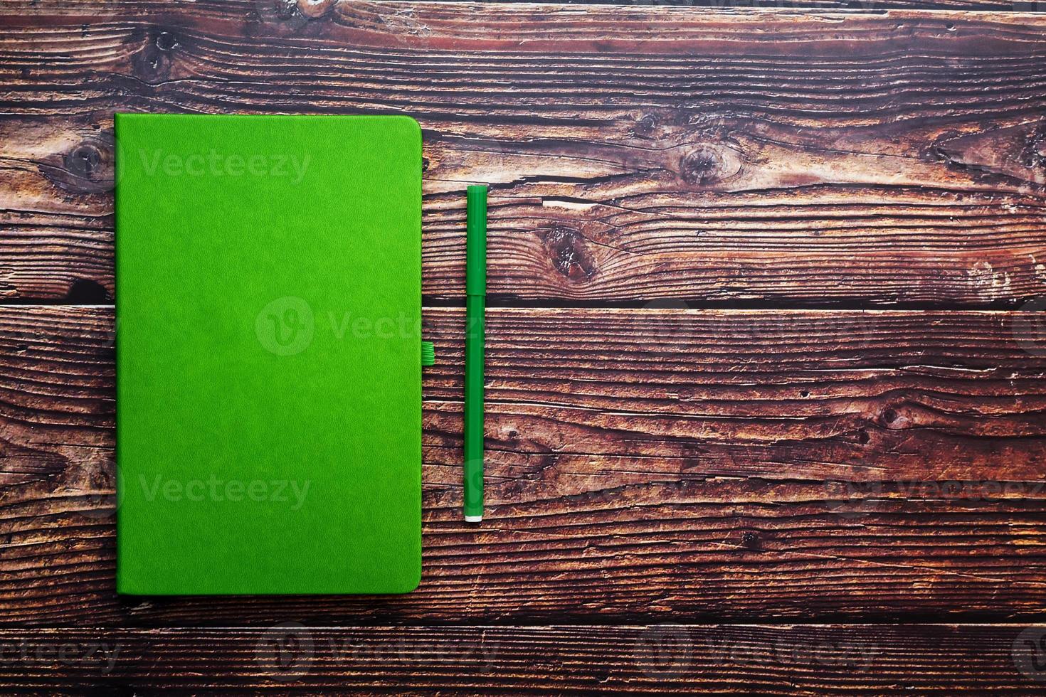 Green Notepad with a felt-tip pen on a brown wooden table, top view. photo