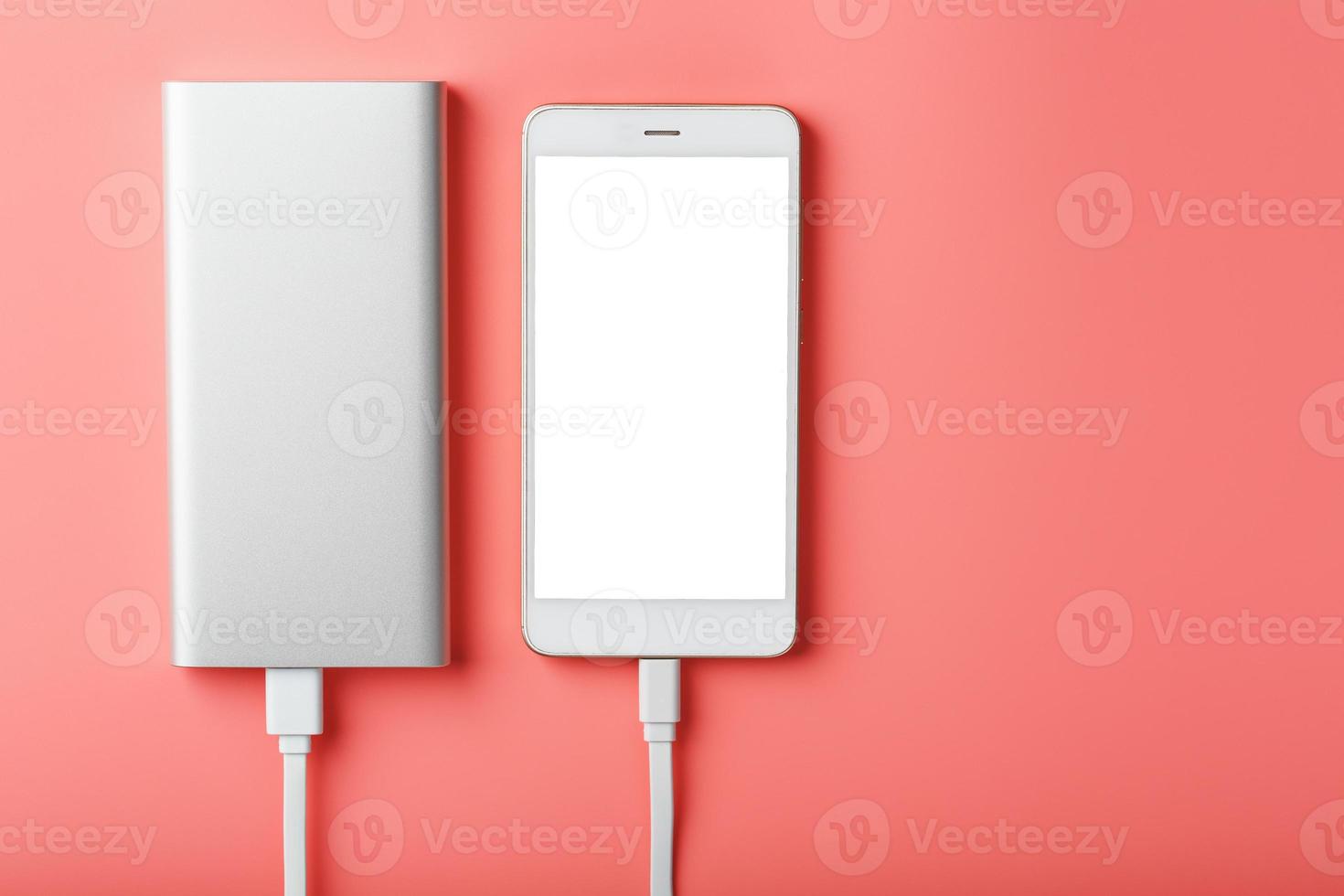 Powerbank charges a smartphone on a pink background. Universal external battery for gadgets Free space and minimalistic composition. photo