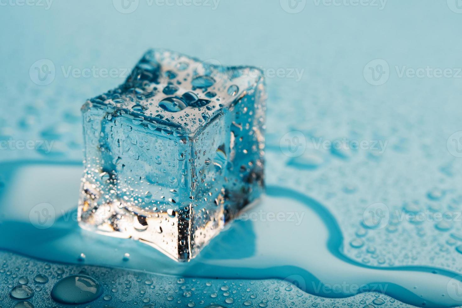 cubo de hielo con gotas de agua sobre un fondo azul. El hielo se está derritiendo. foto