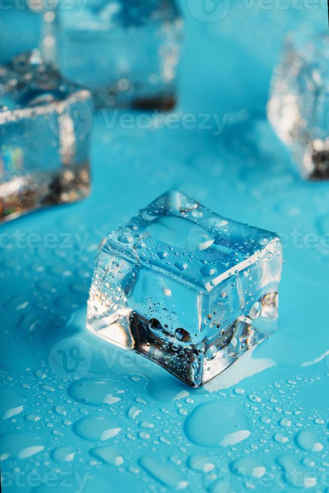 los cubos de hielo están esparcidos con gotas de agua esparcidas sobre un fondo azul. de cerca. foto