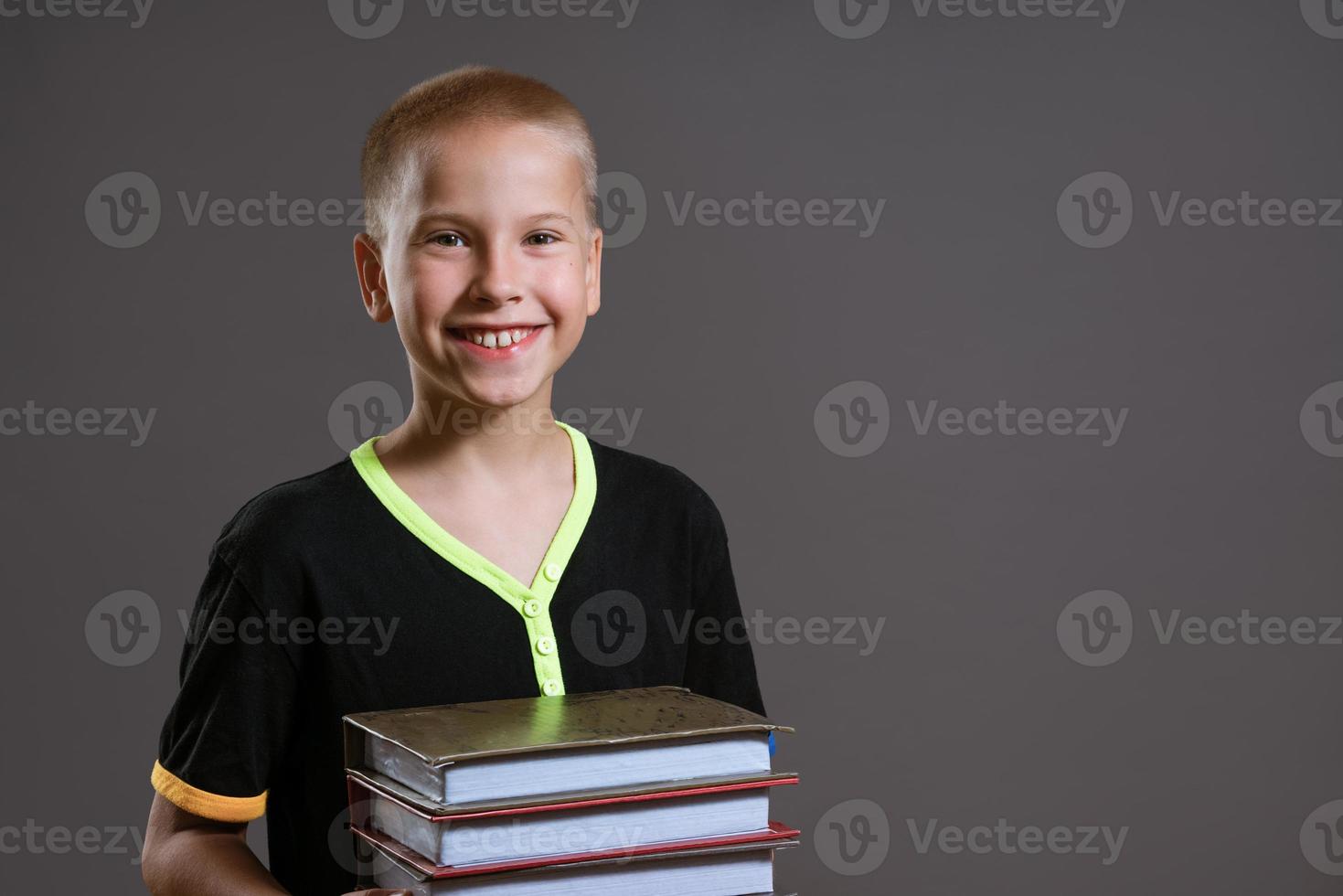 Cheerful boy holding a stack of books on a gray background photo