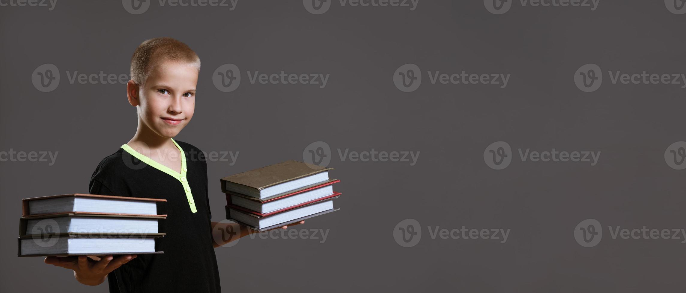 Cute boy holding stacks of books on gray background photo