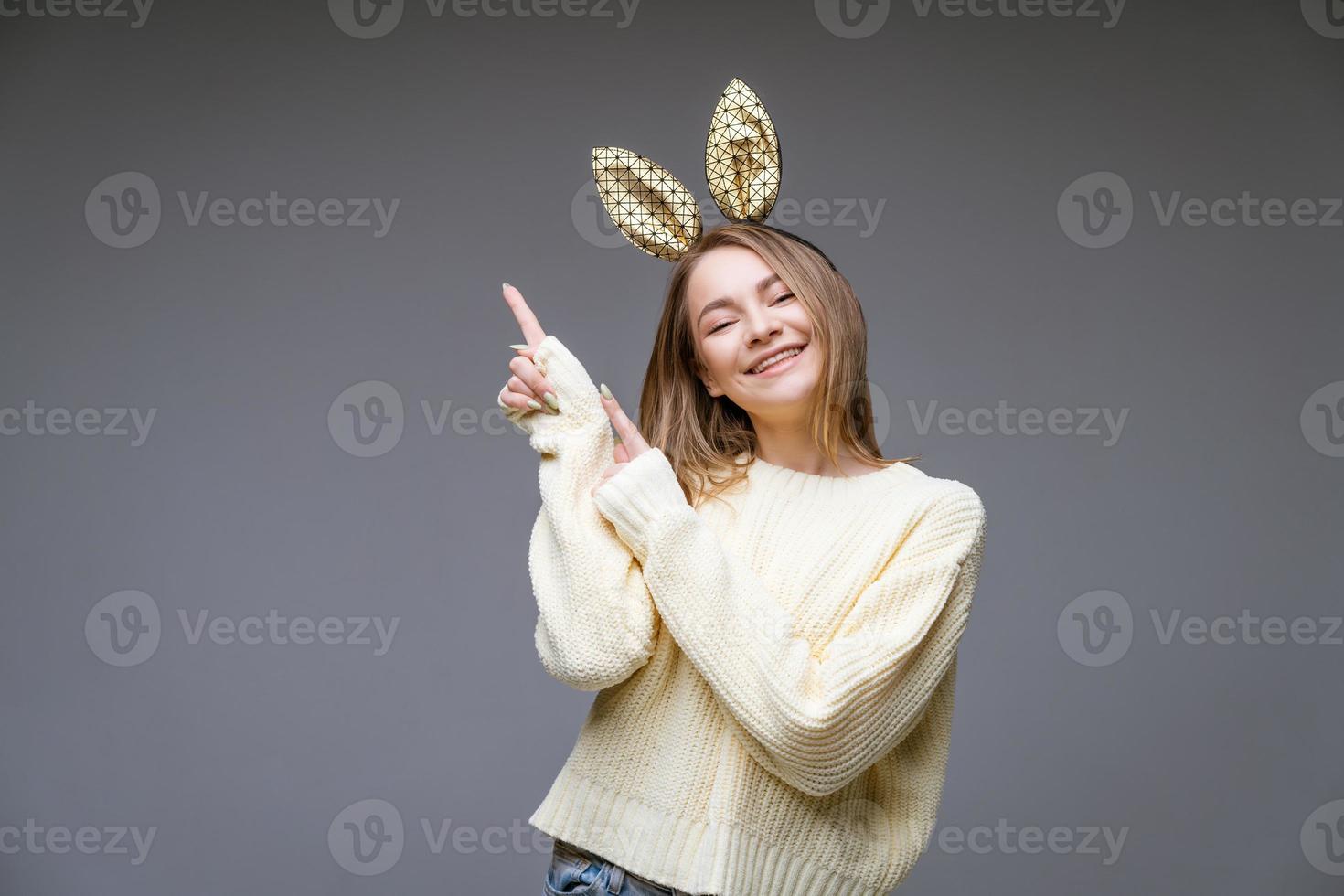 beautiful young woman in bunny ears shows her finger to side on background photo