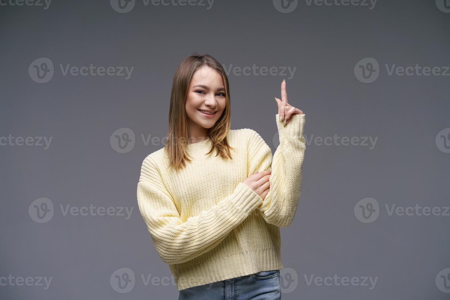 una joven alegre mostrando los pulgares hacia arriba con un suéter amarillo de fondo gris foto