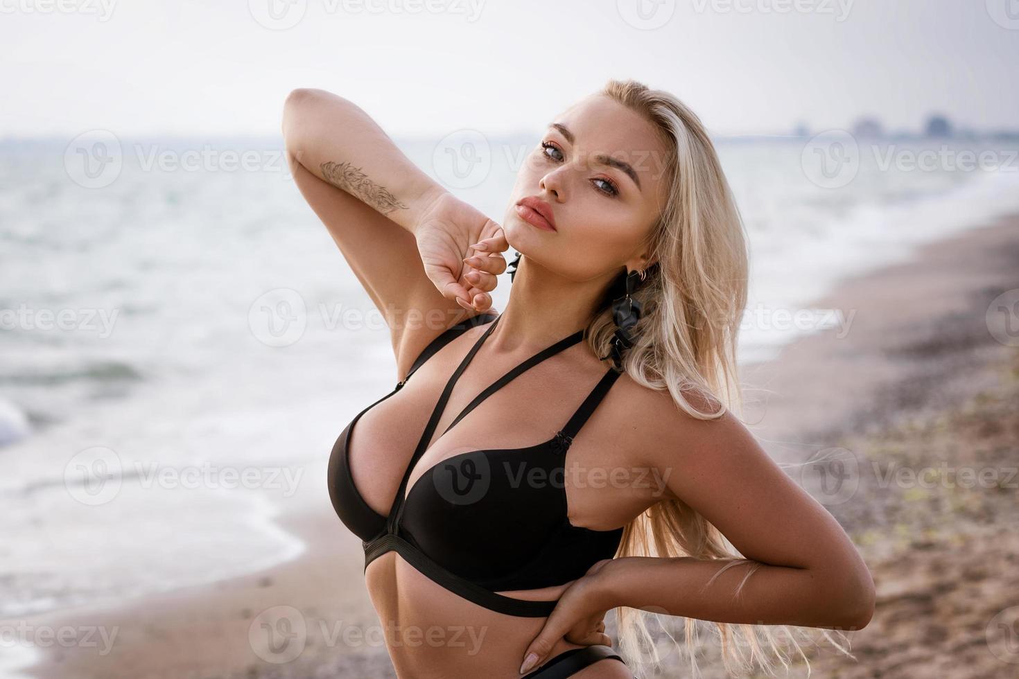 Beautiful woman in black swimsuit posing on the shore photo