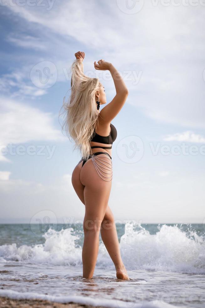 Beautiful woman in black swimsuit posing on the shore photo