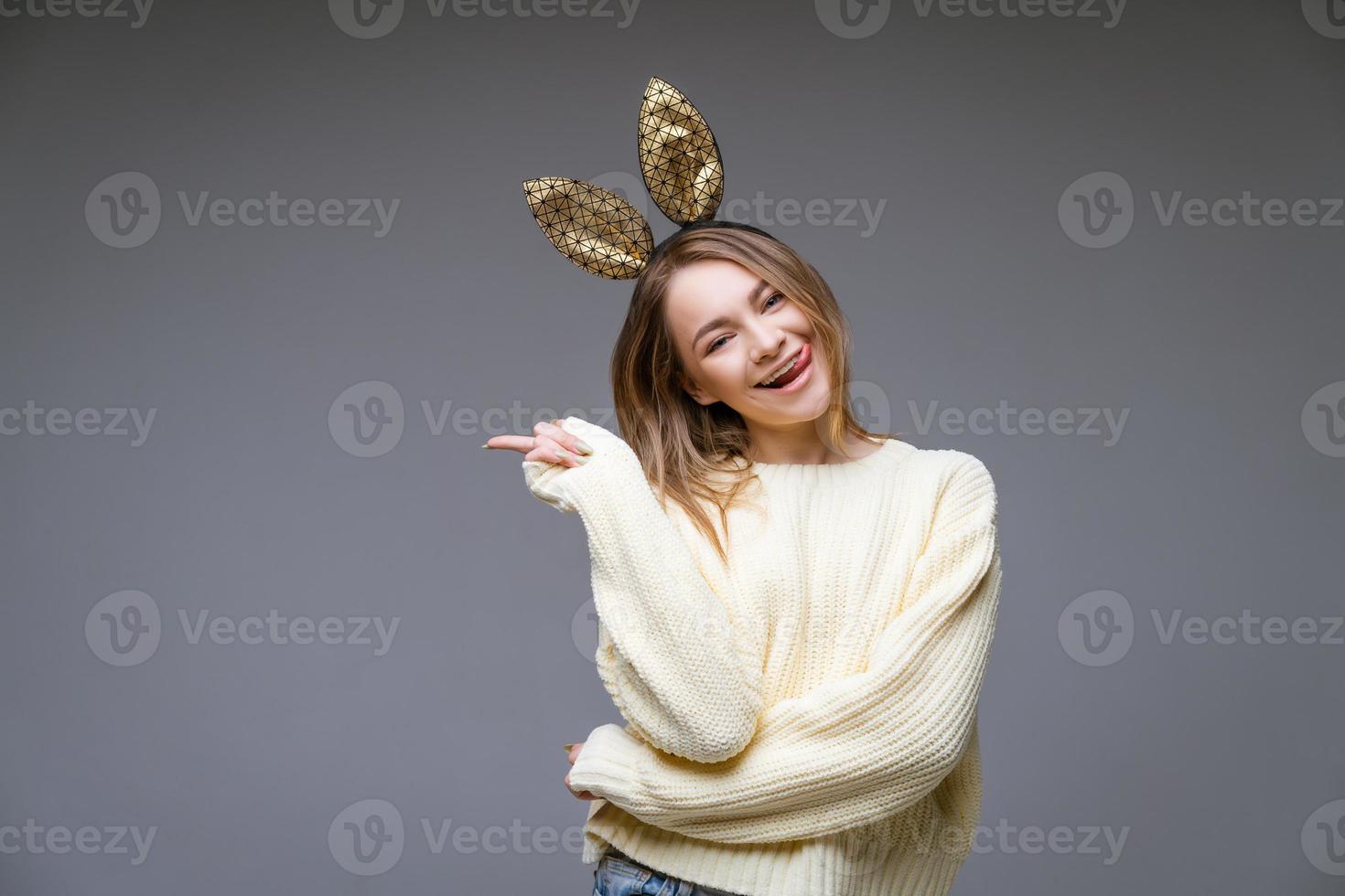 Young woman in rabbit ears shows tongue and finger to the side on background photo