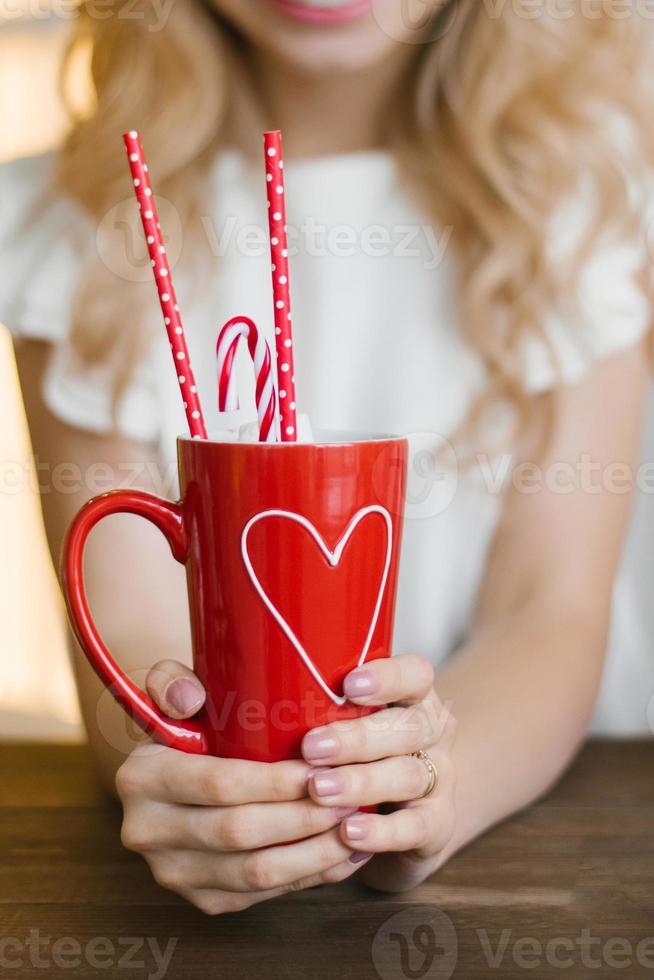 A red mug with a heart pattern with cocoa and paper tubes in the hands of a woman. Valentine's Day Concept photo