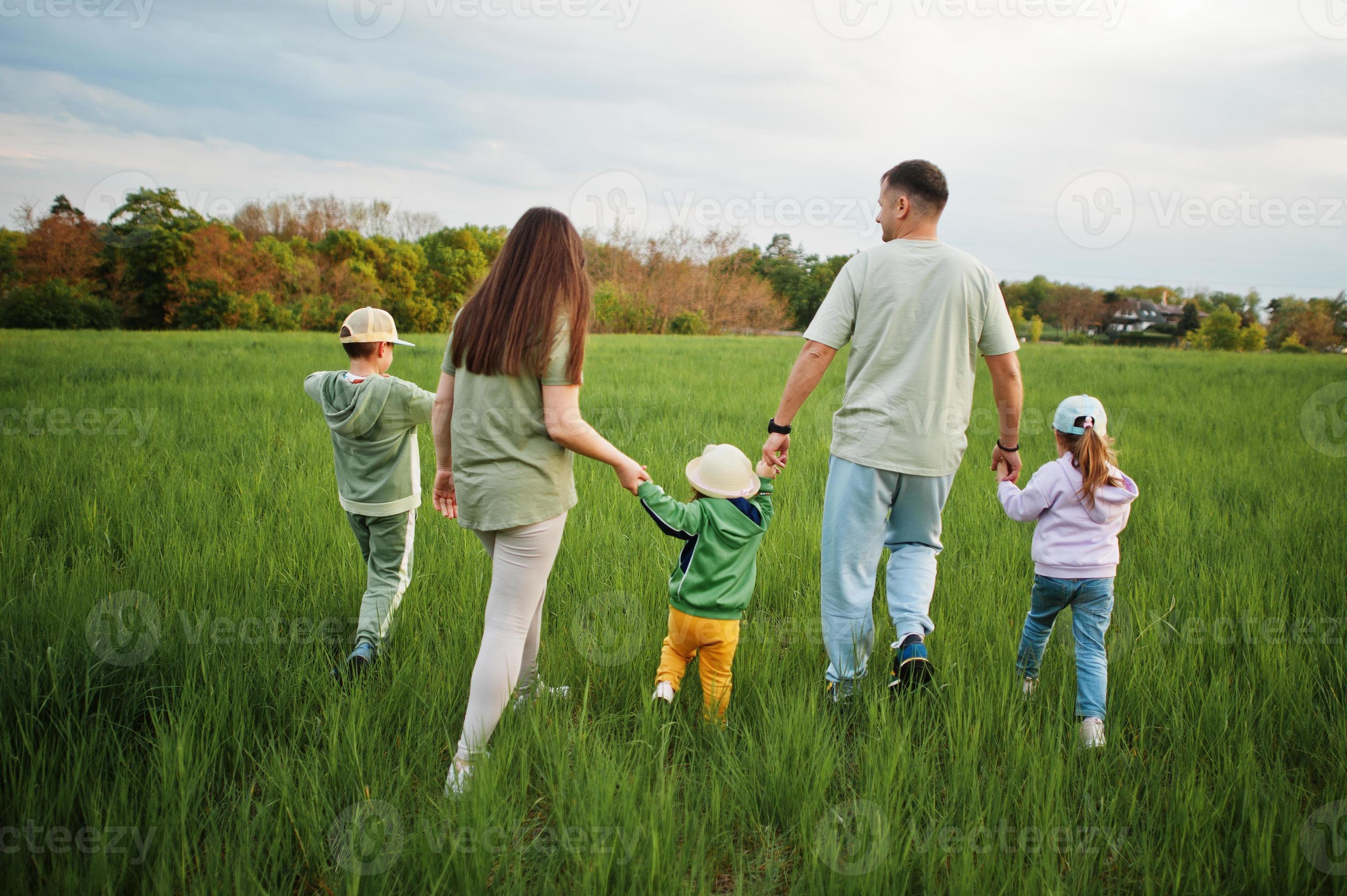 Back Of Walking Parents With Three Kids Having Fun Together At Meadow back-of-walking-parents-with-three-kids-having-fun-together-at-meadow