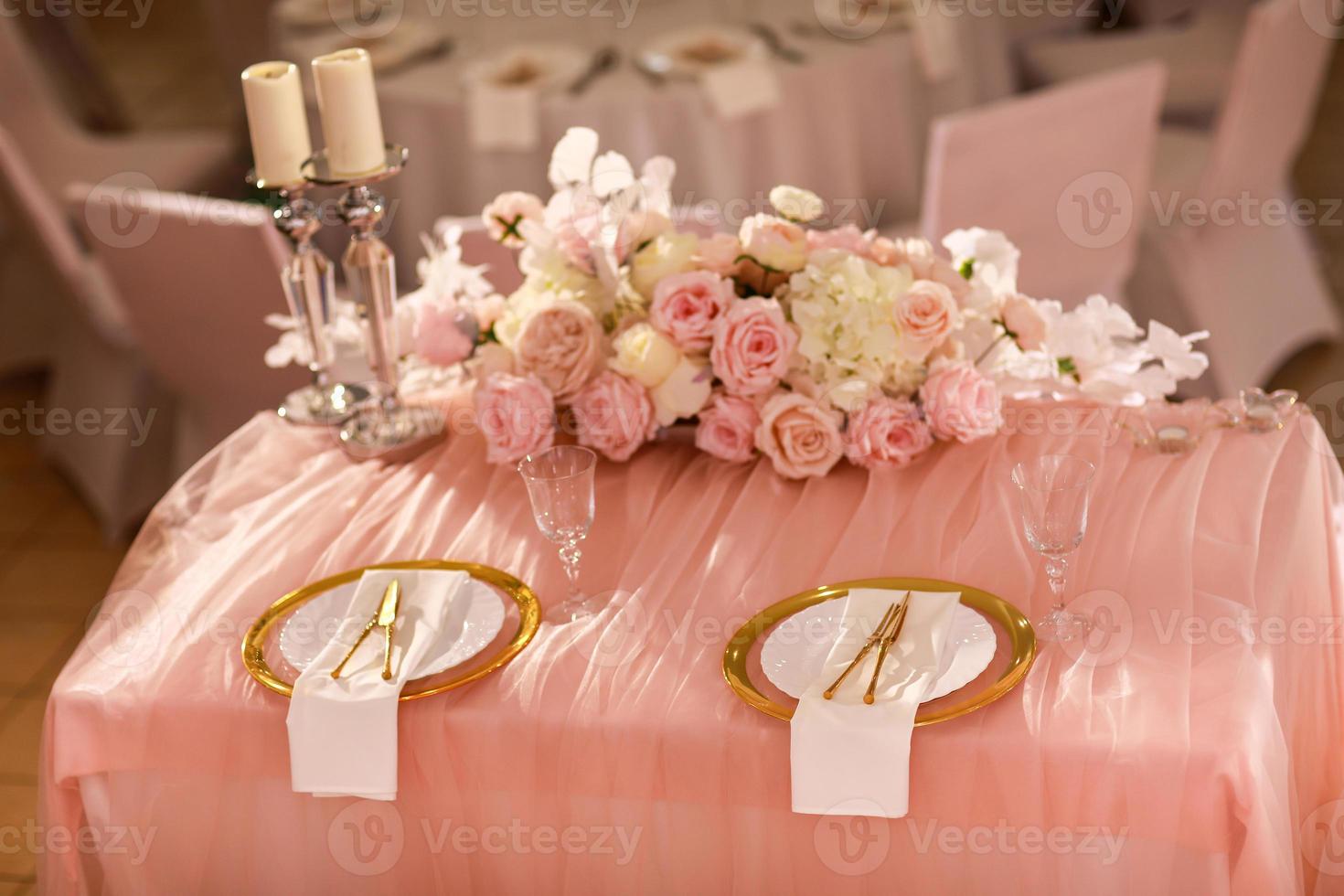 table decoration with pink tablecloth, crystal candlesticks with candles and white pink flowers in restaurant . stylish wedding day. setting table with gold plate, fork and knife photo
