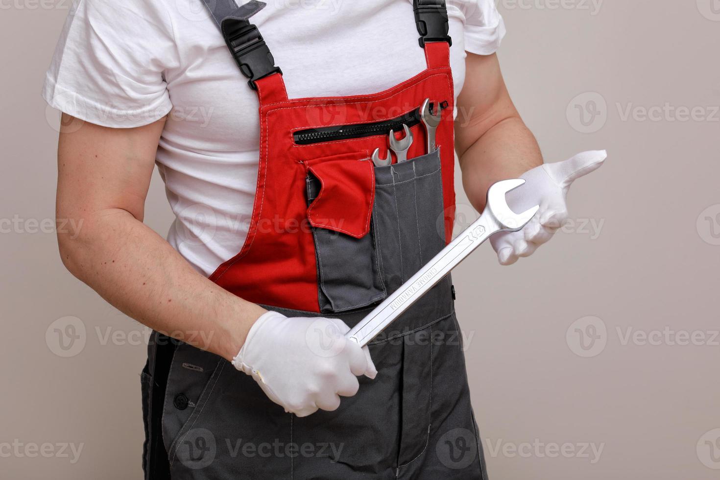 reparador con un mono rojo y gris, sosteniendo una llave en la mano, de pie sobre un fondo blanco. servicio de mantenimiento. concepto de construcción. foto