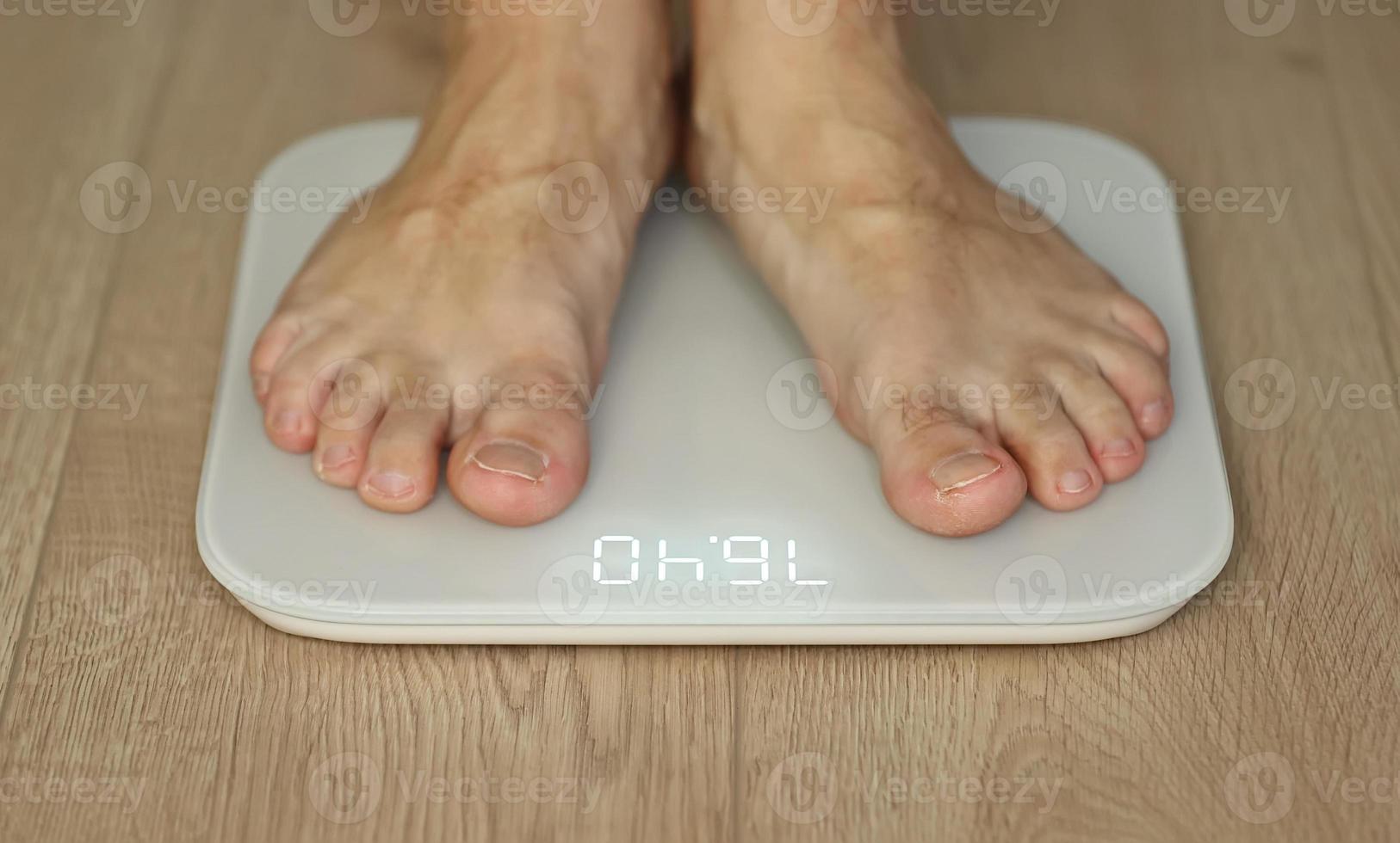 Man weighing himself  male bare feet stepping on white digital floor scales at home close up view. Measuring weight, control, wellness and diet concept photo