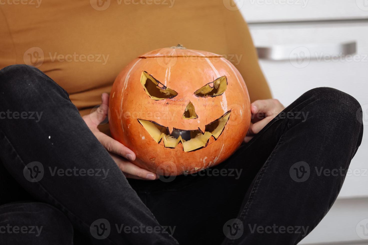 Crop view of adult man sitting on the floor in the kitchen with carved halloween pumpkin. pumpkin jack-o-lantern, indoors. Trick or trunk. Happy Halloween day.selective focus. photo