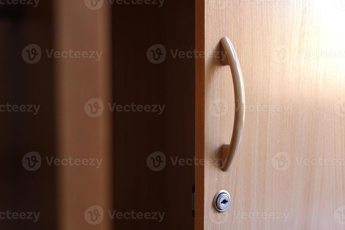 Opened wooden cabinet door with handle and metal keyhole, horizontal photo. Design element, office furniture, curved handle with glare. Storage and organization of space photo