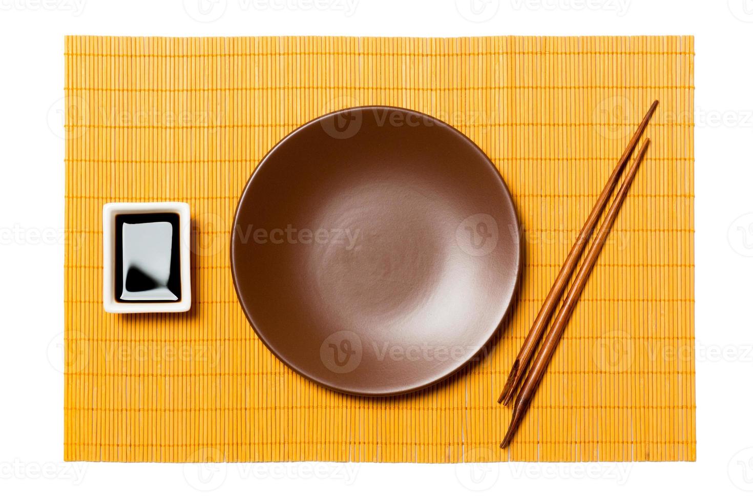 Empty round brown plate with chopsticks for sushi and soy sauce on yellow bamboo mat background. Top view with copy space for you design photo