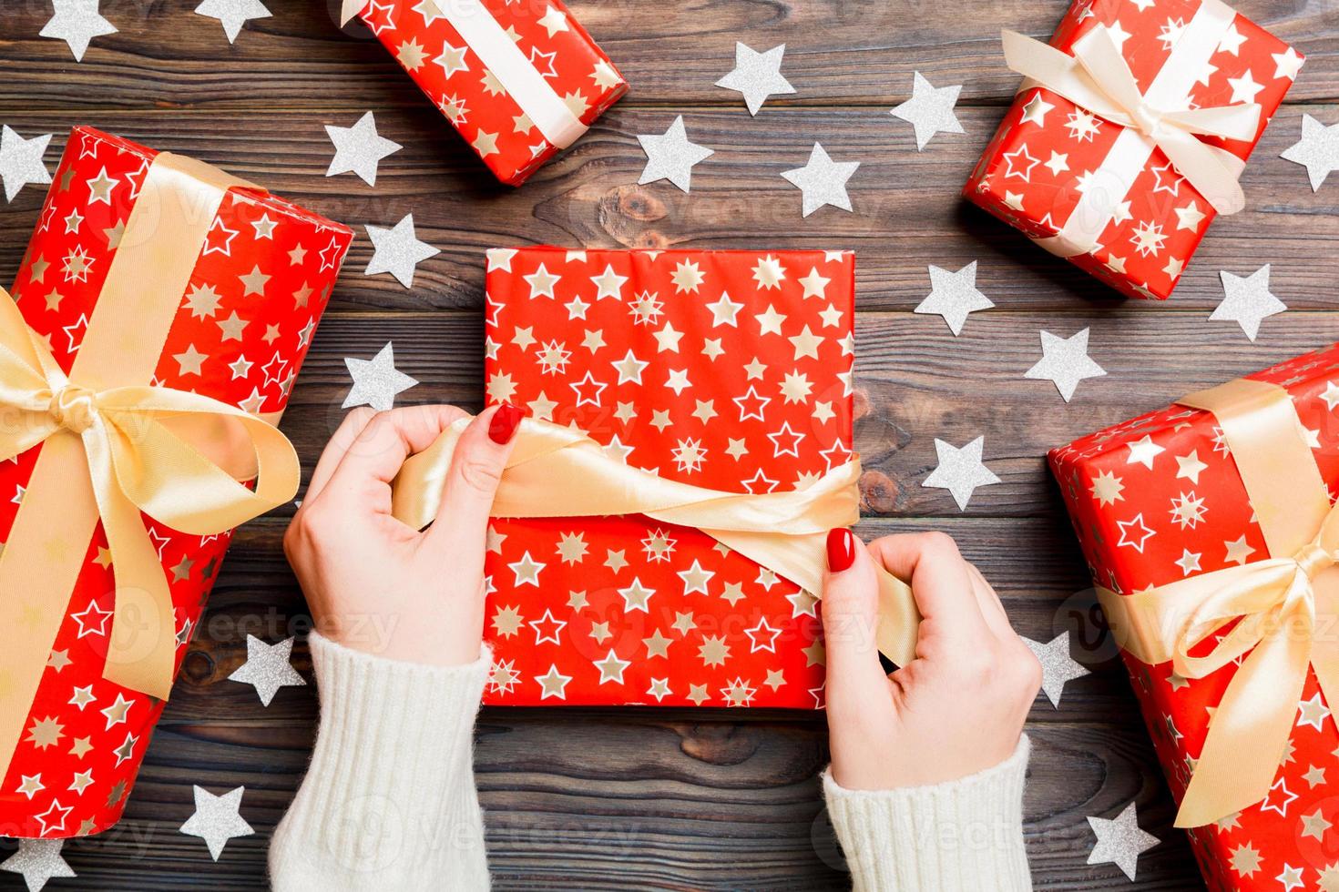 Top view of female hand tie up New Year present on festive wooden background. Gift boxes and snowflakes. Christmas time concept photo