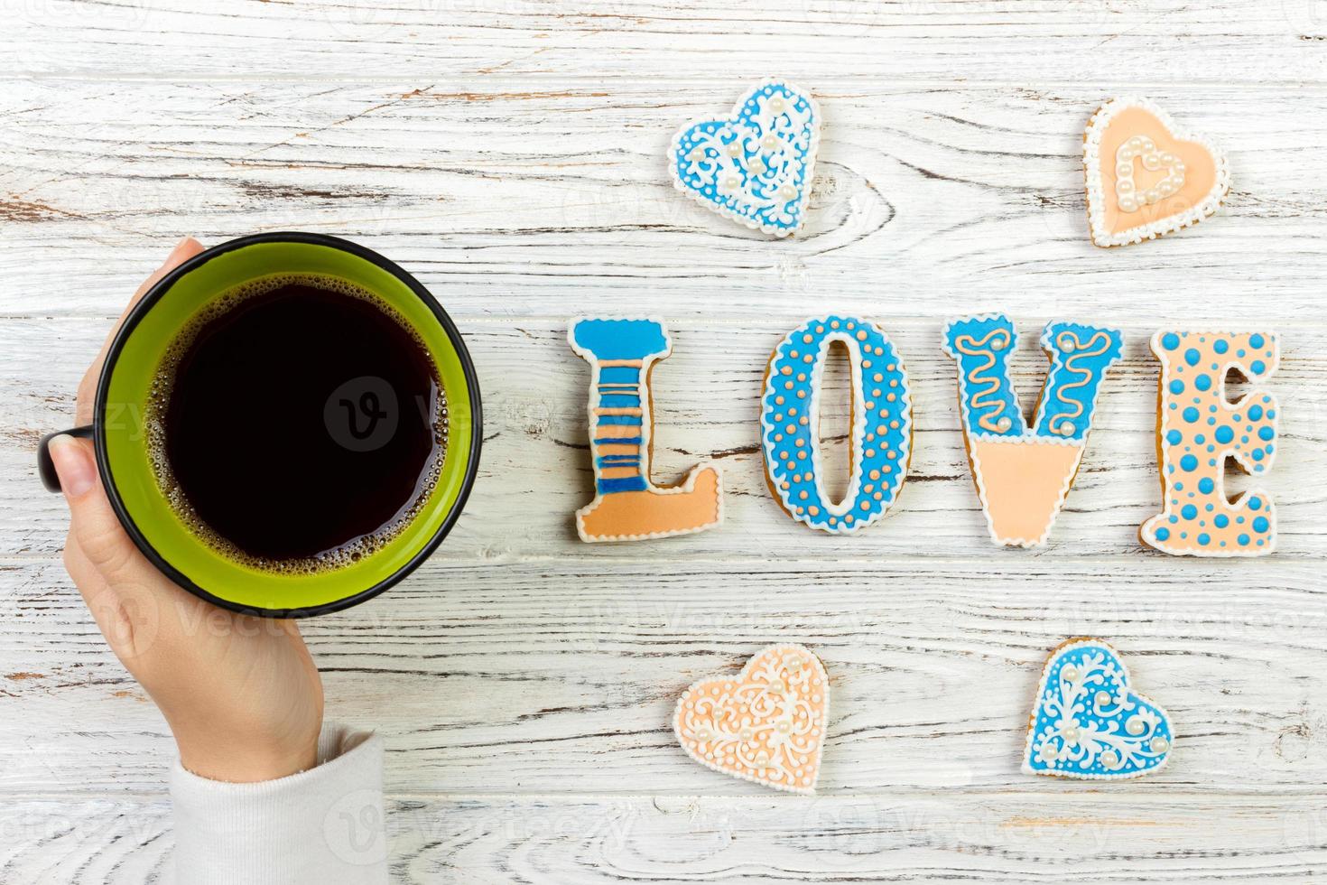 manos femeninas con café y galletas en forma de corazón sobre una mesa de madera, vista superior. concepto de amor foto