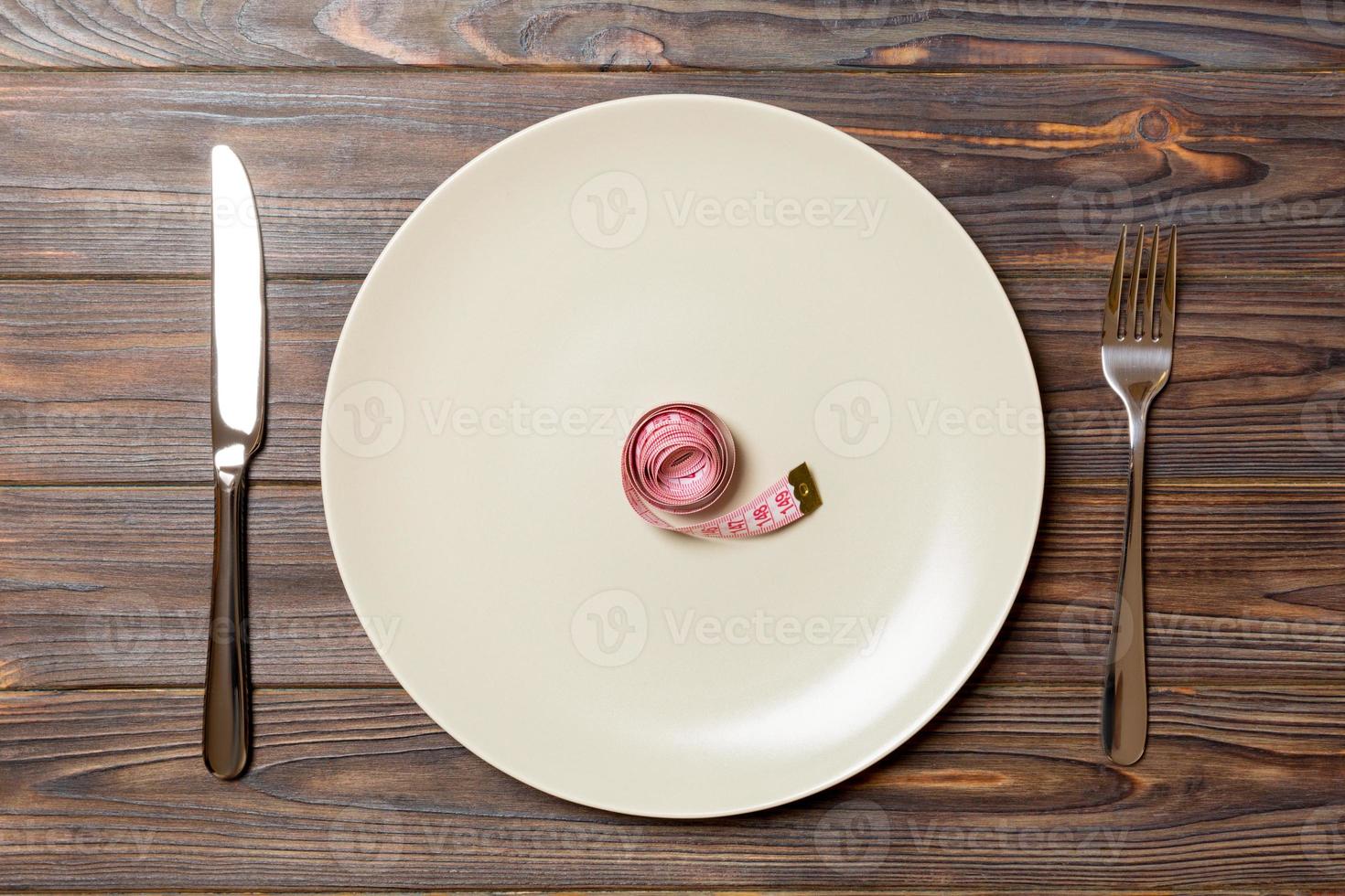 Round plate with measure tape inside with fork and knife on wooden background. Top view of obesity concept photo