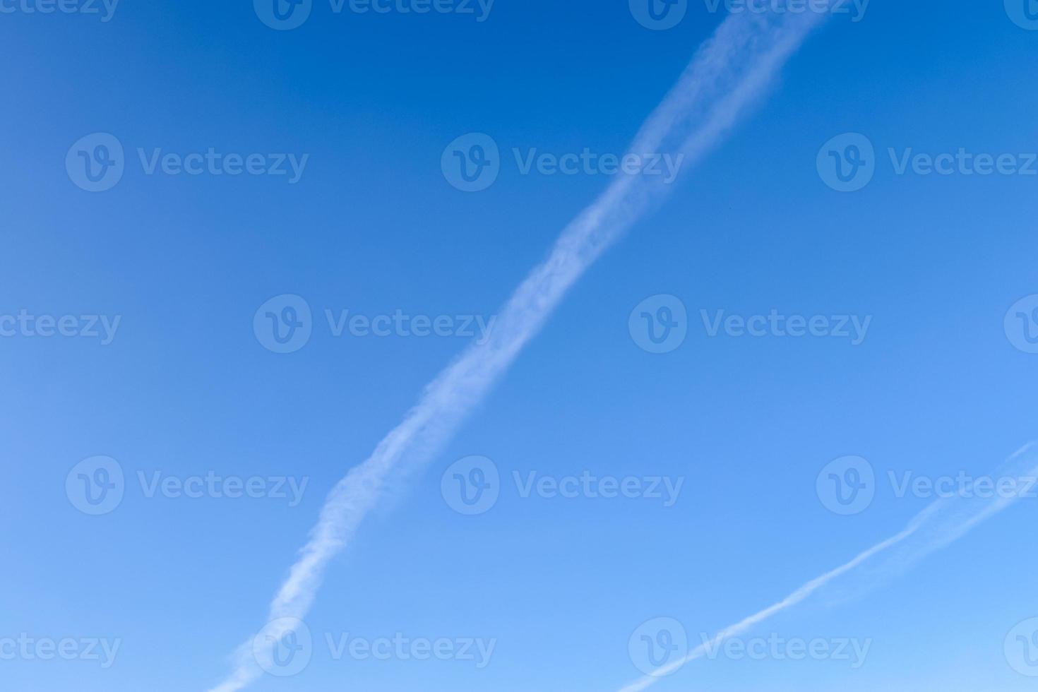 Aircraft condensation contrails in the blue sky inbetween some clouds photo