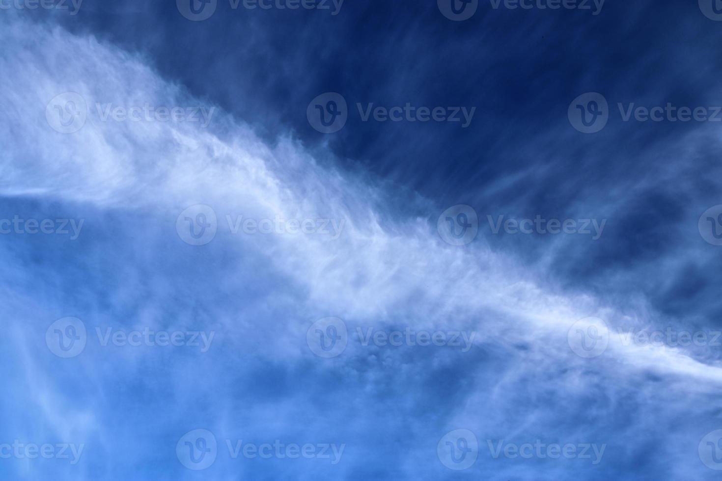 Aircraft condensation contrails in the blue sky inbetween some clouds photo