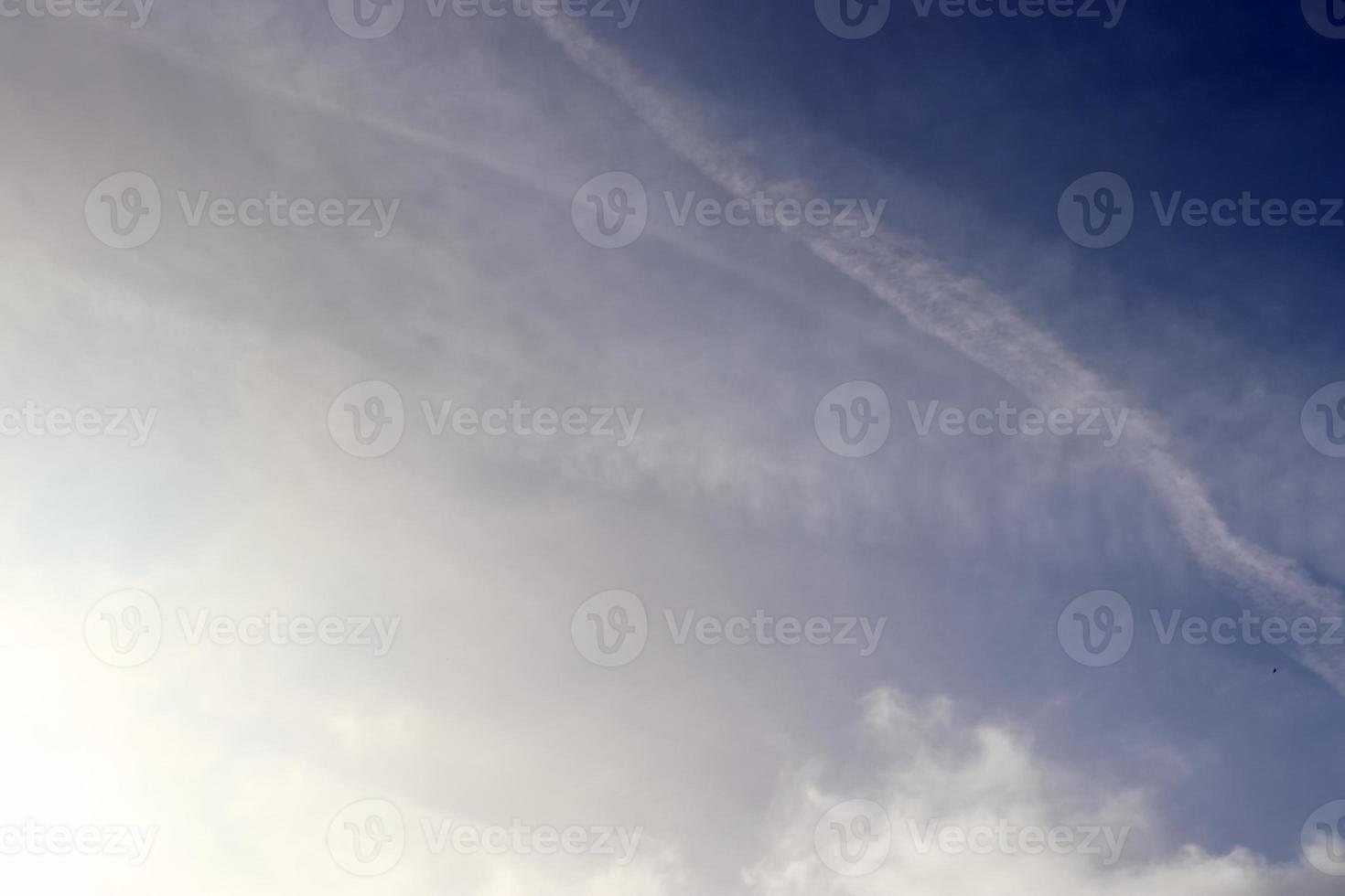 Aircraft condensation contrails in the blue sky inbetween some clouds photo