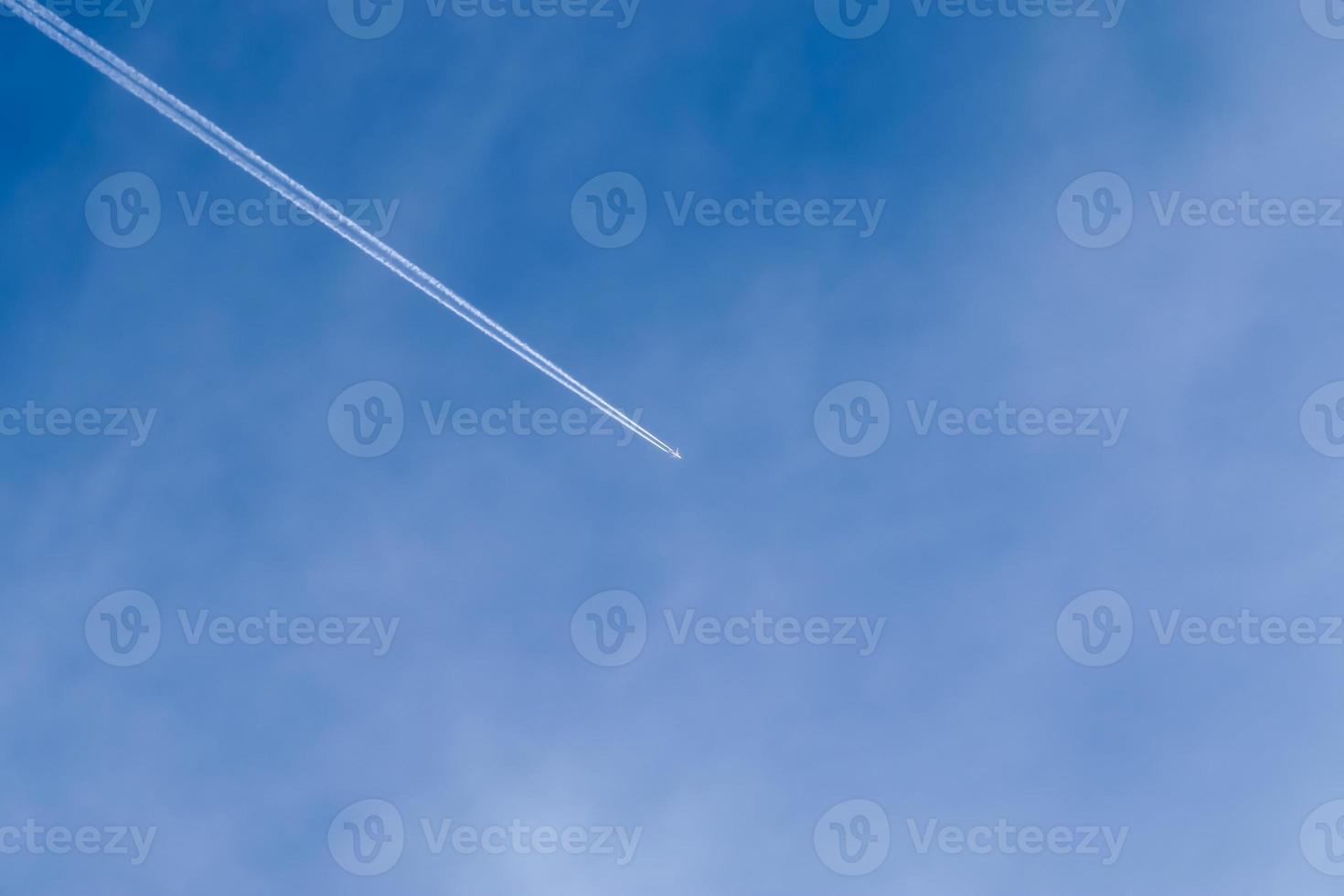 Aircraft condensation contrails in the blue sky inbetween some clouds photo