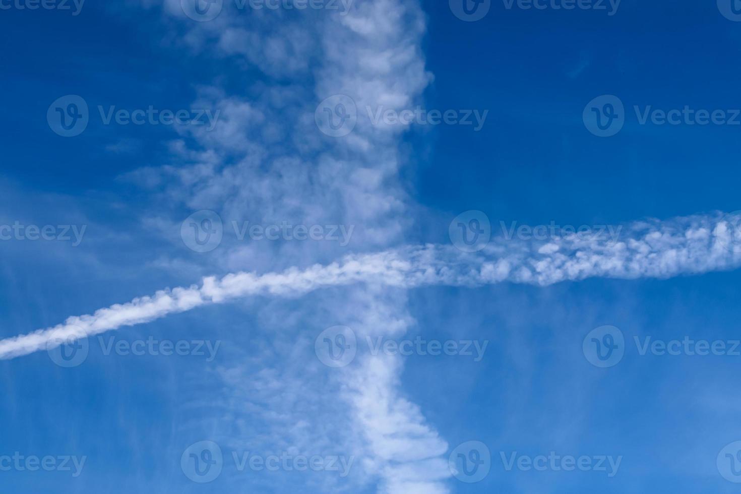 Aircraft condensation contrails in the blue sky inbetween some clouds photo