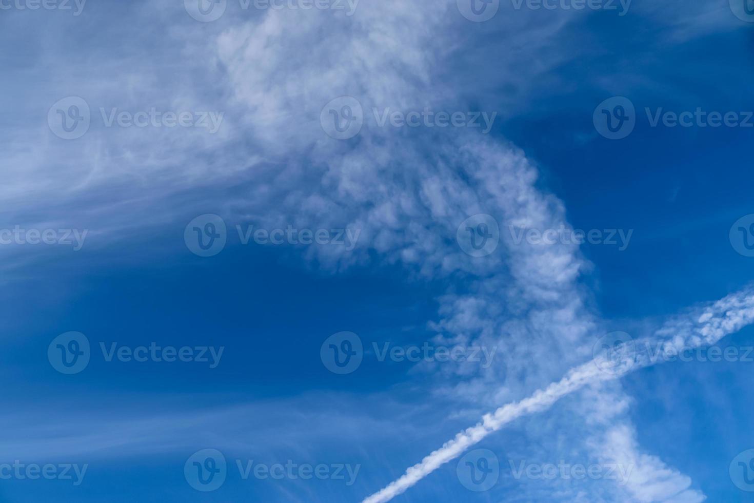 Aircraft condensation contrails in the blue sky inbetween some clouds photo