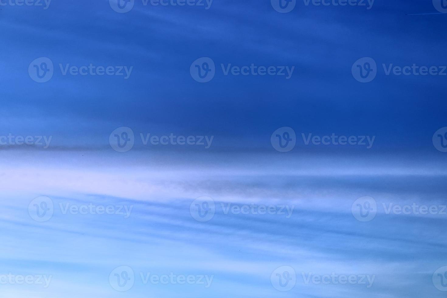 Aircraft condensation contrails in the blue sky inbetween some clouds photo