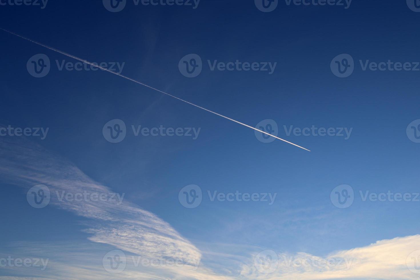 Aircraft condensation contrails in the blue sky inbetween some clouds photo