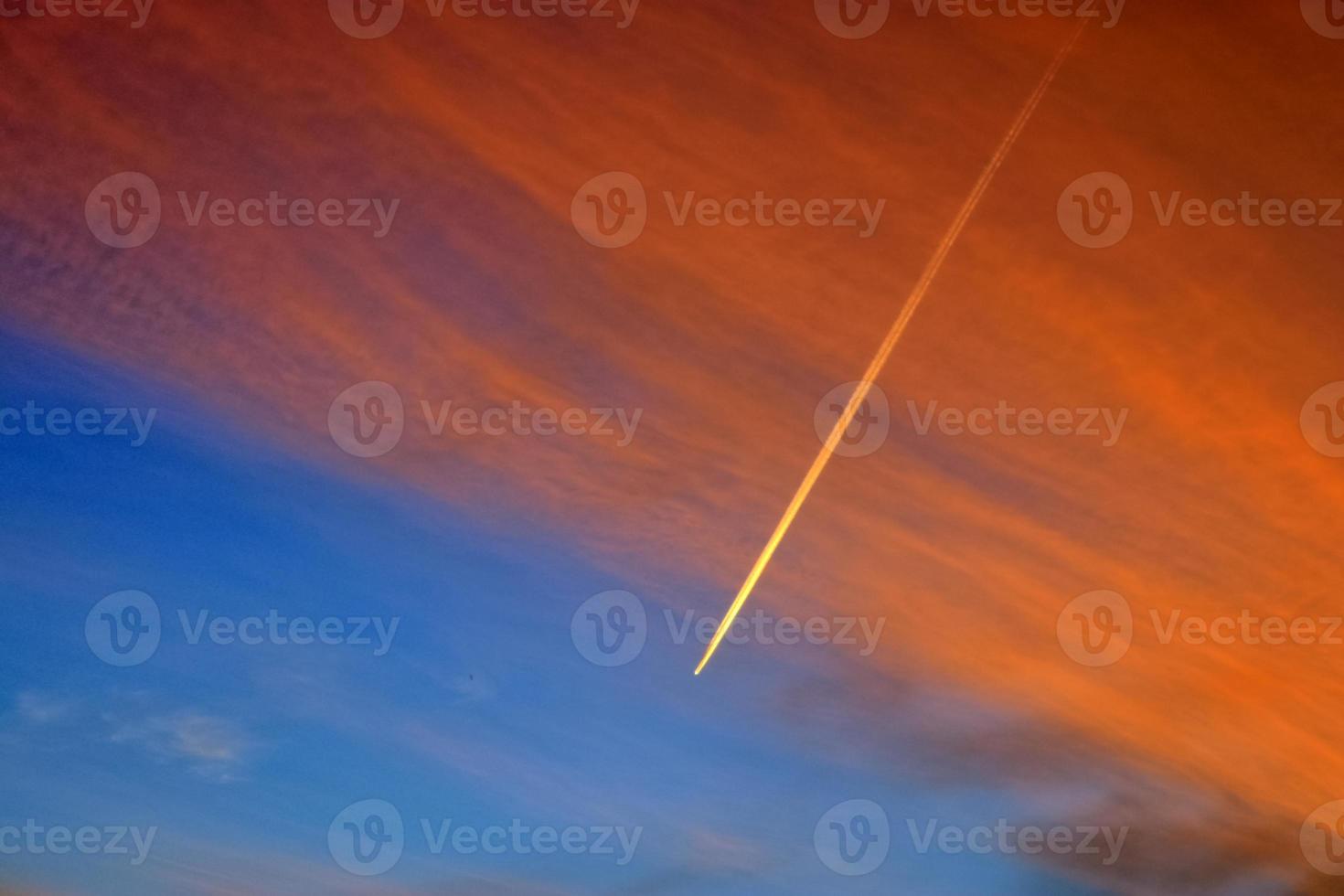 Aircraft condensation contrails in the blue sky inbetween some clouds photo