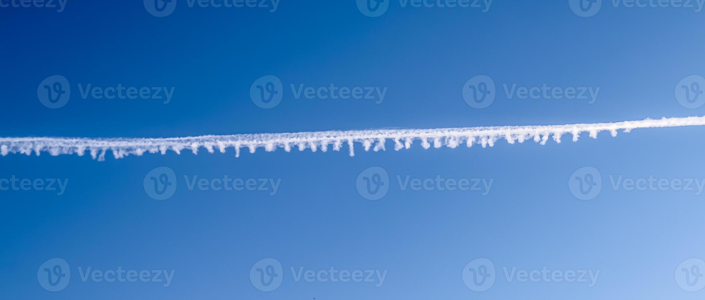 Aircraft condensation contrails in the blue sky inbetween some clouds photo