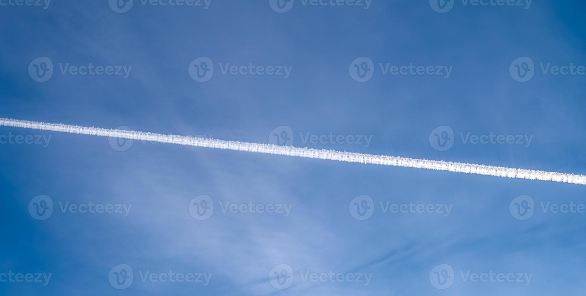 Aircraft condensation contrails in the blue sky inbetween some clouds photo